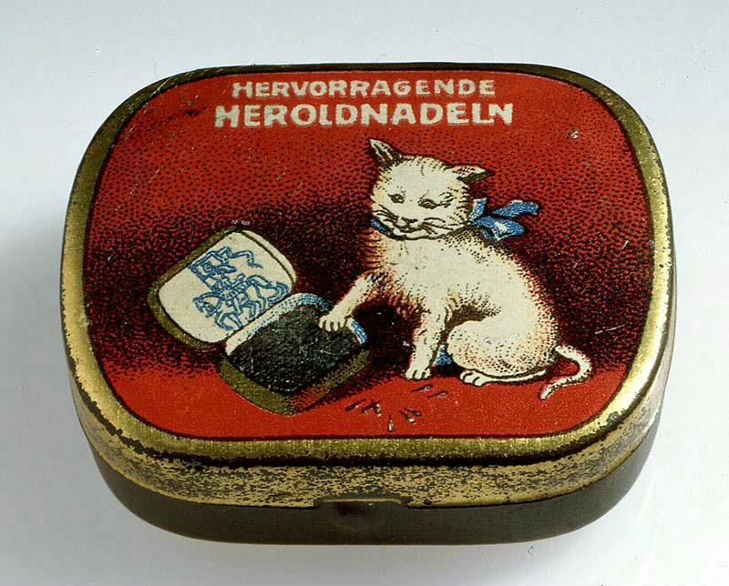 A tin for gramophne needles, decorated with a picture of a cat playing with the needles