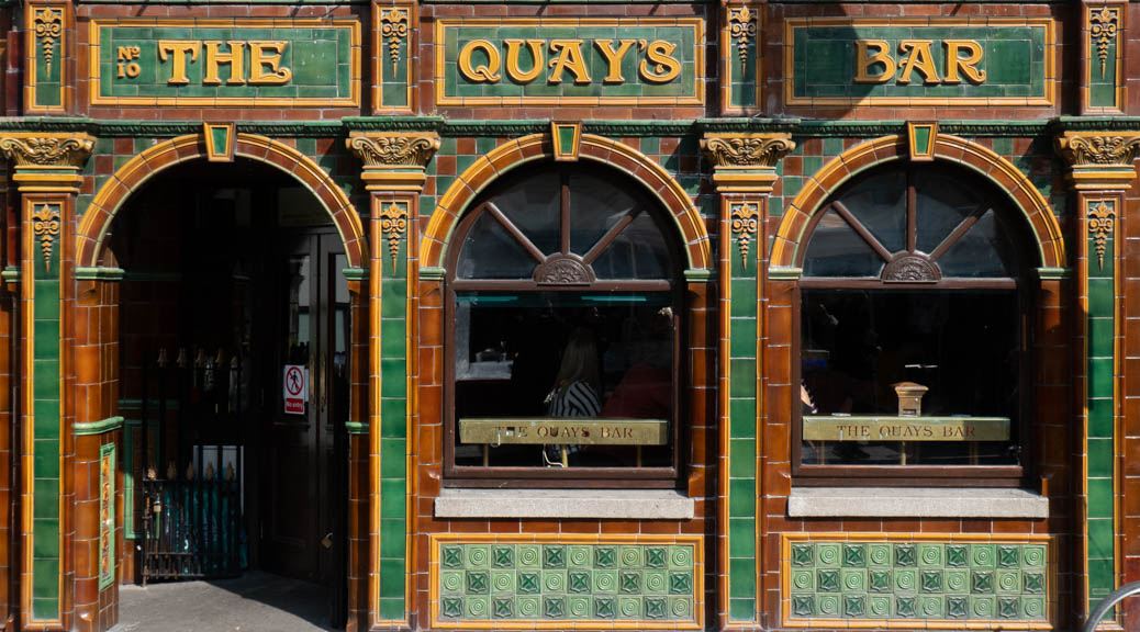 The ground-floor Temple Bar façade of The Quay's Bar, Dublin: a pub facade, tiled in green, brown, and yellow, with an arched doorwy and two arched windows